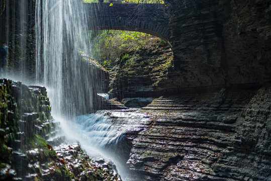 Rainbow falls cascading in Watkins Glen state park New York, Stone arch bridge in background
