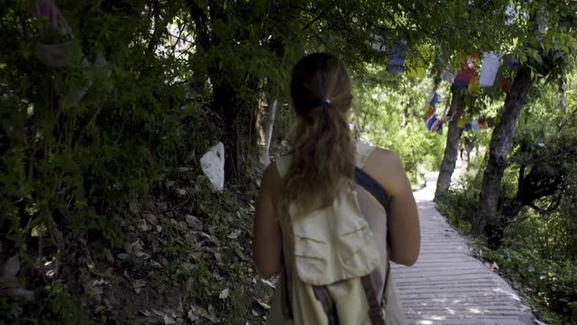 Back view of female traveler walking on religion footpath in forest. Branches and trees decorated colorful buddhist flags. Macleod Ganj, Dharamsala, India