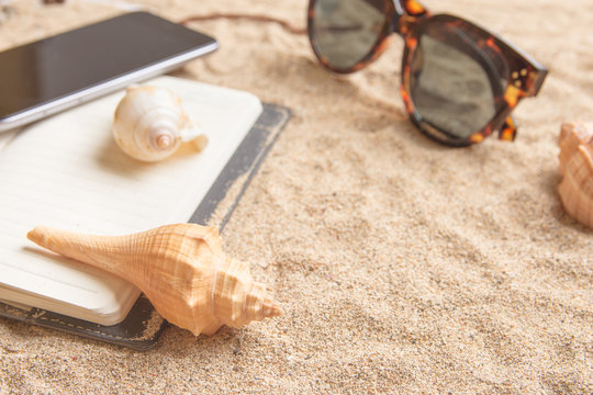 Daily planner on a sandy beach with shells and sunglasses.