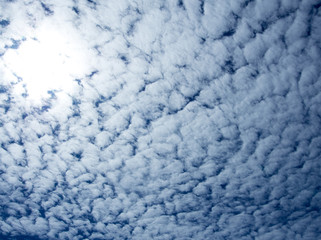 White fluffy clouds in the bright blue sky with light from the Sun