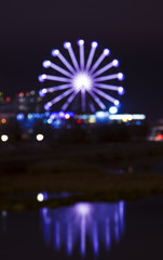 Vibrant blue colored ferris wheel bokeh reflected on water