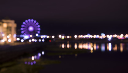 Vibrant city lights and ferris wheel bokeh with reflection on water