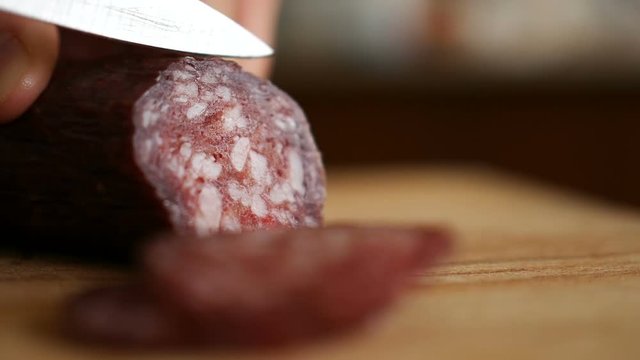 Man cuts into thin slices fatty sausage. Shooting closeup. Chef cutting salami with a knife on a wood board close up.