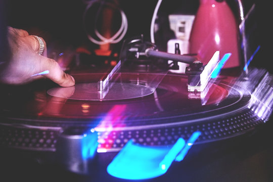 Club DJ hand playing mixing music on vinyl turntable at party nightlife lights with long exposore
