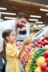 Serious handsome bearded father teaching daughter to pick up fruits at farmers market
