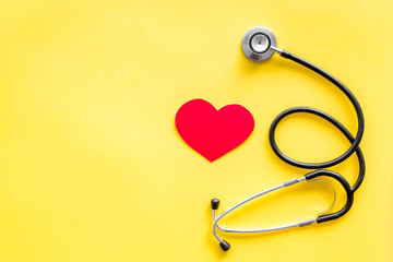 Health care concept. Stethoscope near heart sign on yellow top view copy space