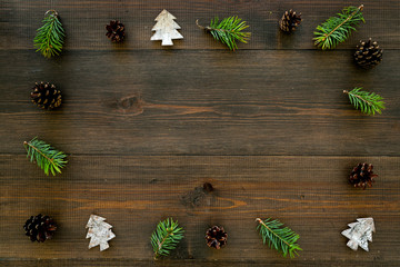 Obraz na płótnie Canvas New Year frame made of pine sprigs, cones, spruce figure, fir oil on dark wooden background top view copy space