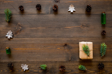 New Year gift decorated with craft paper and pine sprout in frame of spruce branch, pine cones, spruce cutout on dark wooden background top view copy space