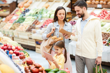 Content modern family in casual clothing buying fresh organic food in farmers market: concentrated...