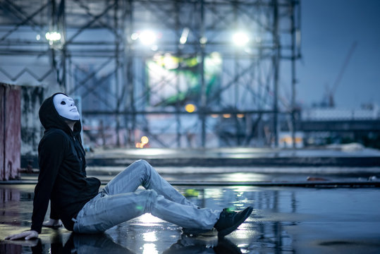 Mystery hoodie man in white mask sitting in the rain looking up at the sky on rooftop of abandoned building. Bipolar disorder or Major depressive disorder. Depression concept