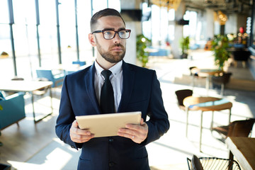 Young pensive owner of cafe in formalwear and eyeglasses searching in the net for some recommendations about menu or interior