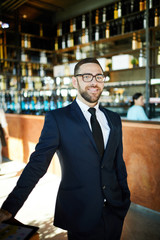 Fototapeta premium Young confident entrepreneur in suit standing on entrance of cafe and meeting guests or new clients