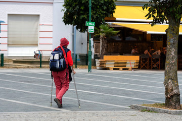 A woman with crutches and a backpack goes along the sidewalk. View from the back.