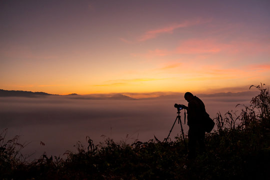 Photographer take photos with mirror camera on peak of mountain. misty landscape, spring orange pink misty sunrise in beautiful valley below.