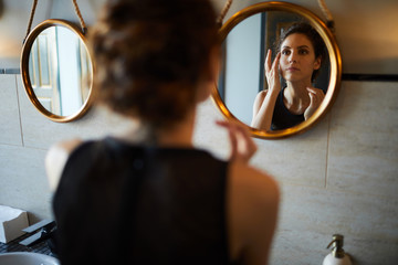 Pretty young woman looking in mirror and refreshing her makeup in lavatory - obrazy, fototapety, plakaty