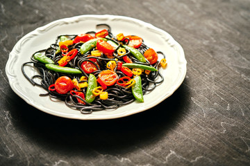fresh delicious black vegan spaghetti with cherry tomatoes, chili pepper, on a white plate