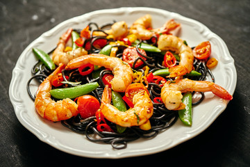 fresh, delicious black spaghetti with grilled shrimps, tomatoes, chilli peppers, on a white plate