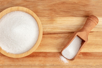 An overhead closeup photo of a bowl and a scoop of white sugar, shot from above on a rustic wooden background with a place for text