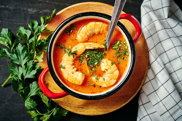 traditional Thai soup with shrimp and coconut milk in a red pot and a spoon with parsley