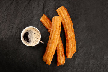 A photo of black coffee in a vintage cup and traditional Spanish porras, a typical Sunday breakfast in Madrid, shot from the top on a dark background with a place for text, weekend morning in Spain