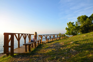 Obraz premium A woman sitting on a bench is watching the sunset over the sea.