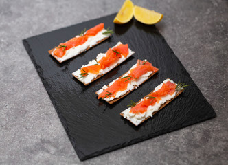 Tasty snack with salmon and soft cheese on a black plate
