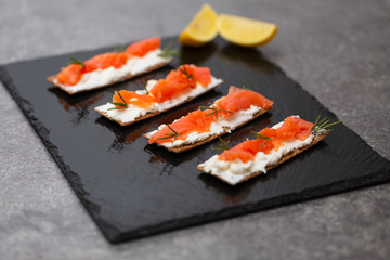 Tasty snack with salmon and soft cheese on a black plate