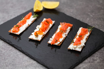 Tasty snack with salmon and soft cheese on a black plate