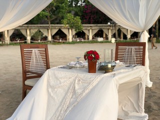 Romantic dinner white table set with red flower on the beach in the early evening