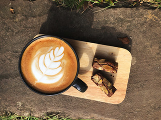 Delicious Breakfast;  Latte art coffee in Black cup and Brownie topped with almond sliced in wooden tray with natural light
