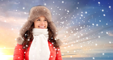 Fototapeta na wymiar people, season and leisure concept - happy woman in winter fur hat outdoors over snow and sky background
