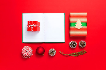 Open notebook with blank pages, gift boxes, fir branches on red background flat lay top view. Christmas planning concept Holiday decorations 2019 Goals. New Year, Christmas, winter decoration