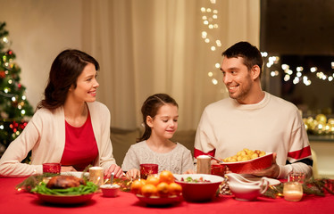 holidays, family and celebration concept - happy mother, father and little daughter having christmas dinner at home