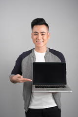 Copy space on his laptop. Good looking young man pointing copy space on his laptop and smiling while standing against grey background