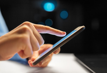 business, deadline and technology concept - close up of businesswoman hands with smartphone at night office