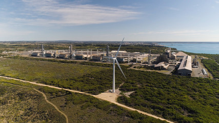 Wide drone shot behind wind turbine with aluminum smelter in background -  Filmed under our CASA ReOC UAV commercial license.