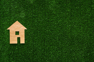 Green energy for home concept. Care for environment. House cutout made of craft paper on green grass background top view copy space