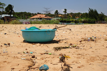 View on a sandy beach near to fishing village with a lot of garbage. Pollution of a coastline. Mui Ne, Vietnam.