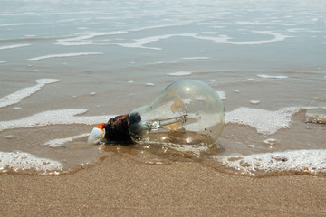 Obraz premium Old light bulb on a sandy beach near to the sea. Pollution of a coastline. Vung Tau, Vietnam.