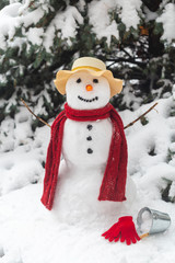 snowman in the forest in Christmas clothes, next to the tree