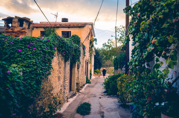 beautiful view in vintage style of narrow alley with  old house, colorful flowers  and a traditional elderly woman dressed in black in a village in crete.