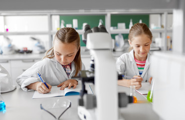 Obraz premium education, science and children concept - kids studying chemistry at school laboratory and writing to workbooks