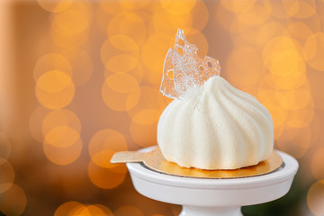 Mini mousse pastry dessert covered with white velour on garland lamps bokeh background. Modern european cake. French cuisine. Christmas theme