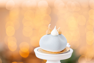 Mini mousse pastry dessert with gray velour on garland lamps bokeh background. Modern european cake. French cuisine. Christmas theme