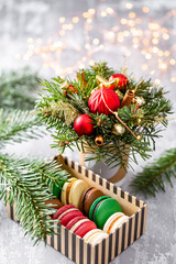 Variety of sweet macaroons in carton box. Fir branches on a gray background. Merry Christmas card. New year mood