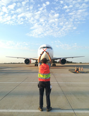 Ground Crew in the signal vest. Aviation Marshall / Supervisor meets passenger airplane at the airport. Aircraft is taxiing to the parking place.