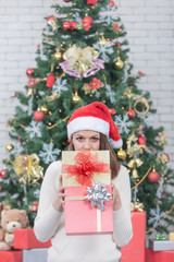 Young and beautiful caucasian woman in red hat and holding gift boxes.There is big decorated christmas tree in background.Concept for good time in christmas festival.