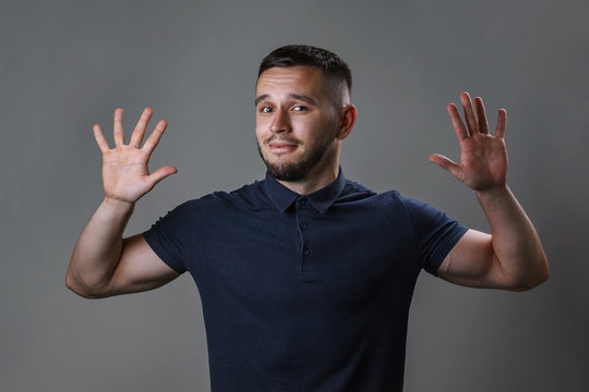 Studio portrait of a young man keep hands up before him with the expression "give up". The concept of harmony, humility, protest, humorous mood.