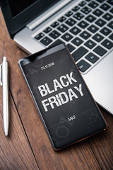 Modern smartphone with black friday banner on the screen lies on wooden desk. Application on screen created in graphic program