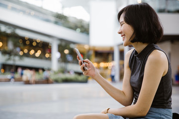 A smiling beautiful asian woman using mobil phone to send sms message.